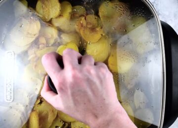 Potatoes and onions in an electric skillet with the lid on.
