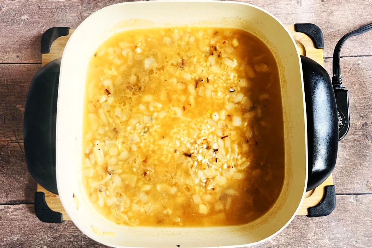 Rice, onion and broth cooking in electric skillet.
