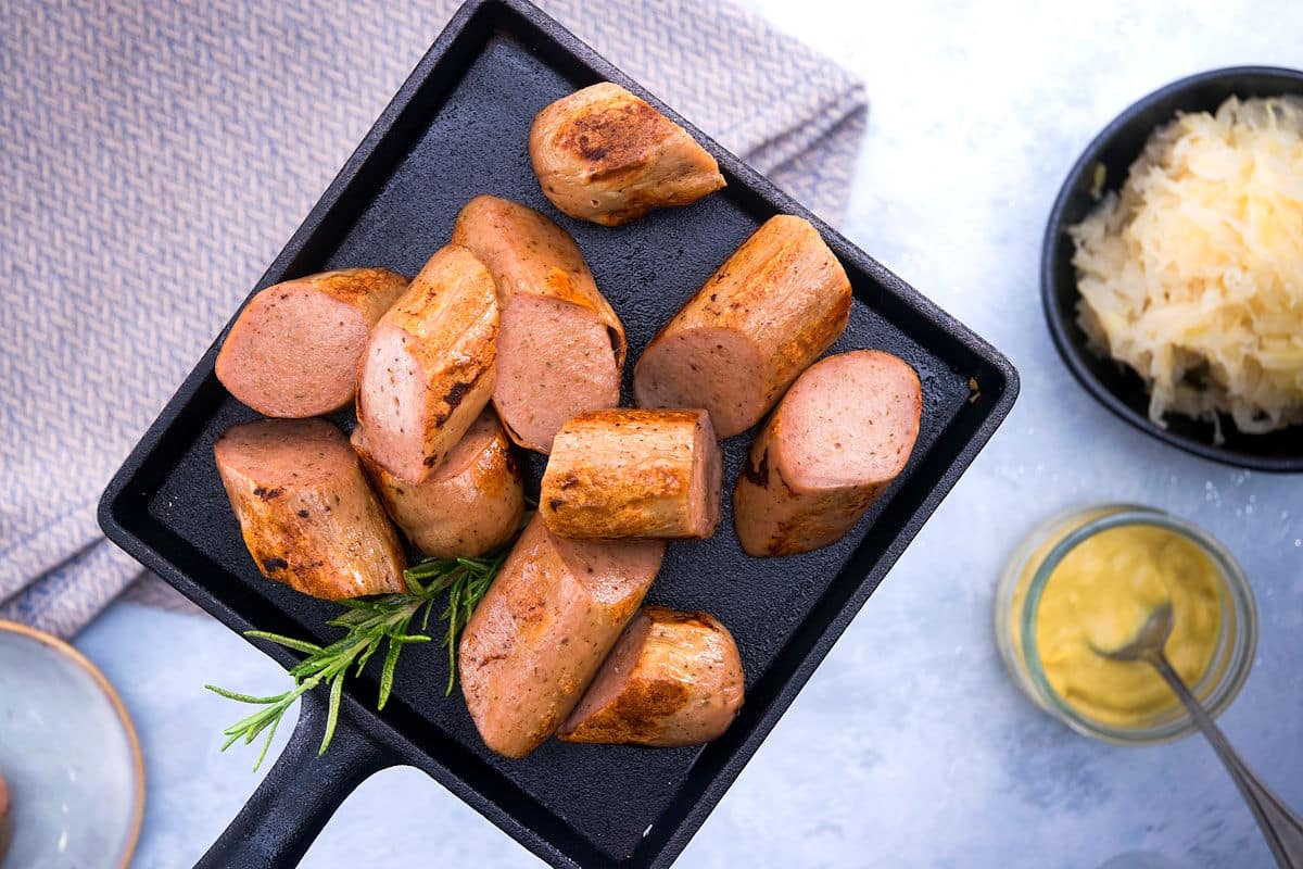 Electric skillet sausage on a cast iron dish with sauerkraut and mustard on the side.