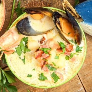 Seafood chowder in a bowl with wooden fish on the side.