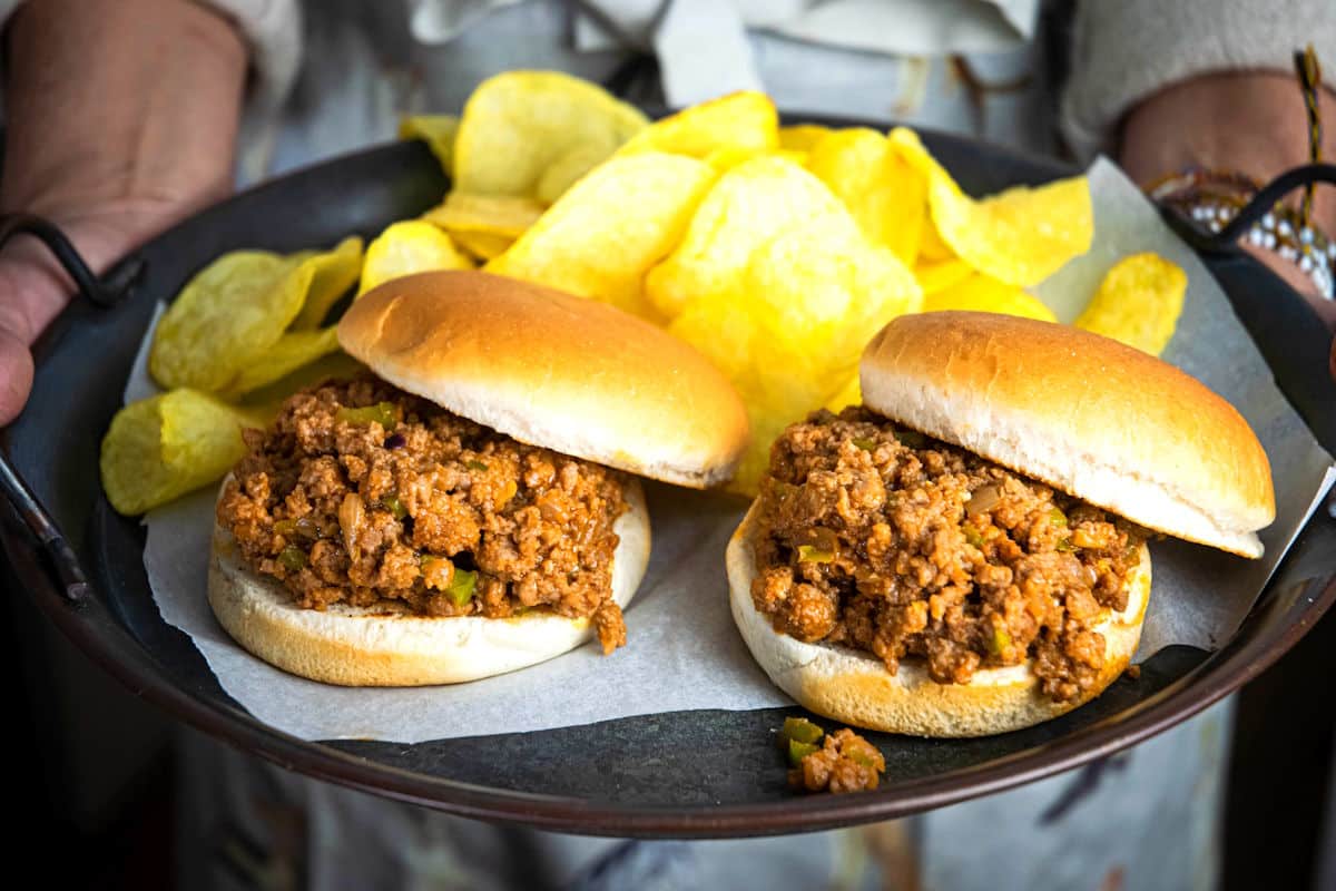 Sloppy Joes on a serving tray in women's hands with chips.
