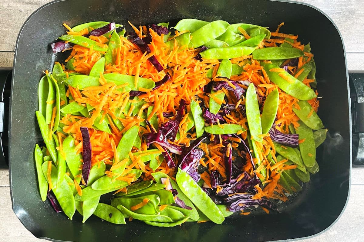 Carrots, snap peas and red cabbage frying in electric skillet.