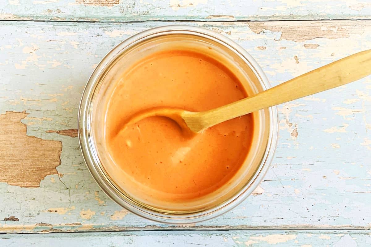 Fish stick sauce in small bowl with small wooden spoon.
