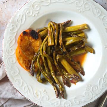 Grilled asparagus and orange slices on white plate.
