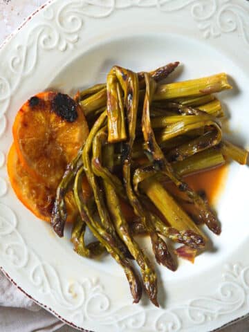 Grilled asparagus and orange slices on white plate.
