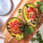 Grilled avocado halves stuffed with pico de gallo on cutting board.