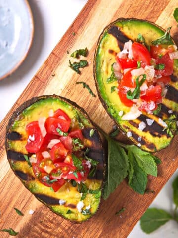 Grilled avocado halves stuffed with pico de gallo on cutting board.