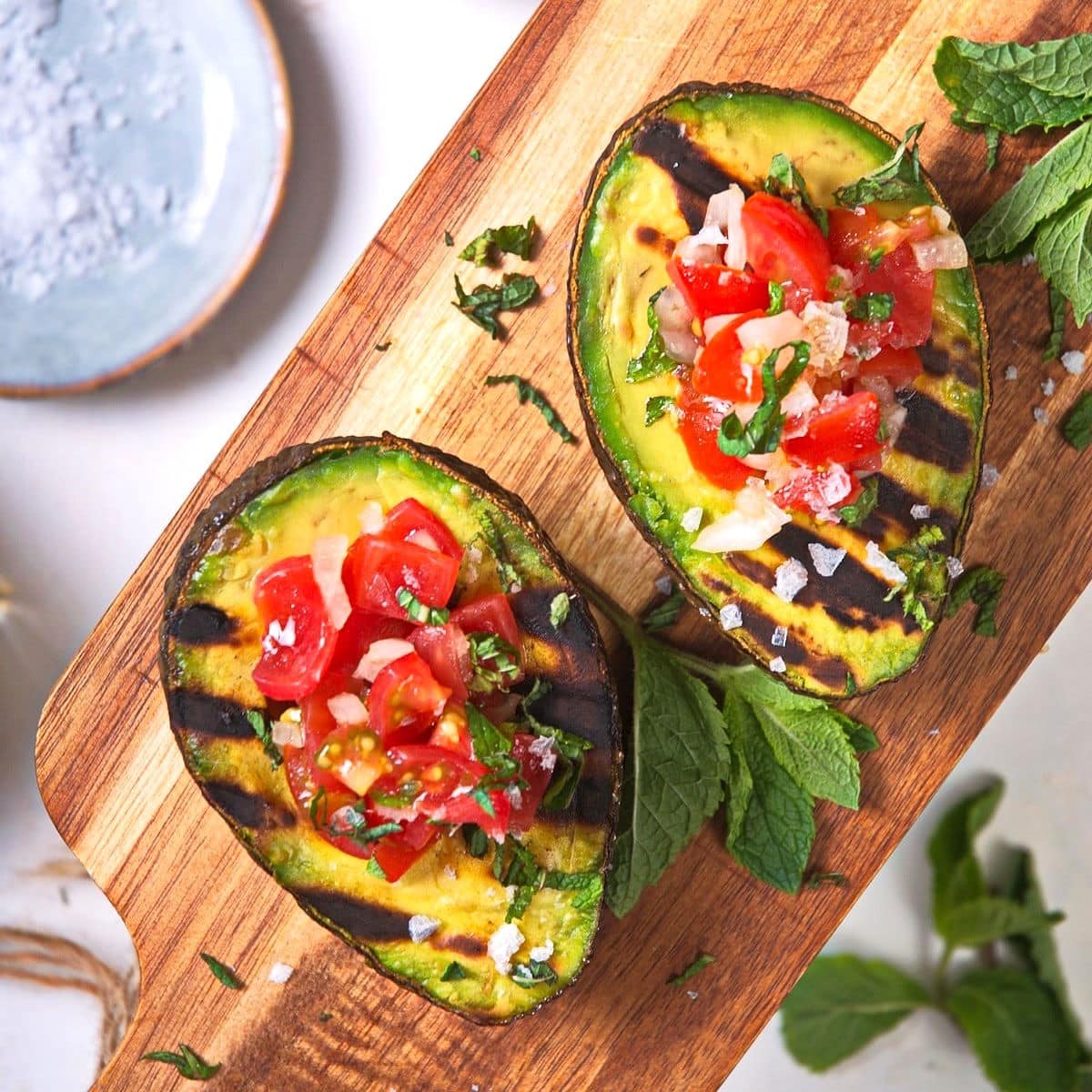 Grilled avocado halves stuffed with pico de gallo on cutting board.