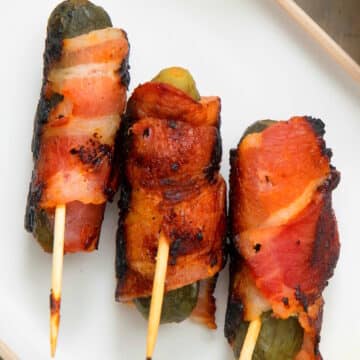 Grilled bacon wrapped pickles on white dish.