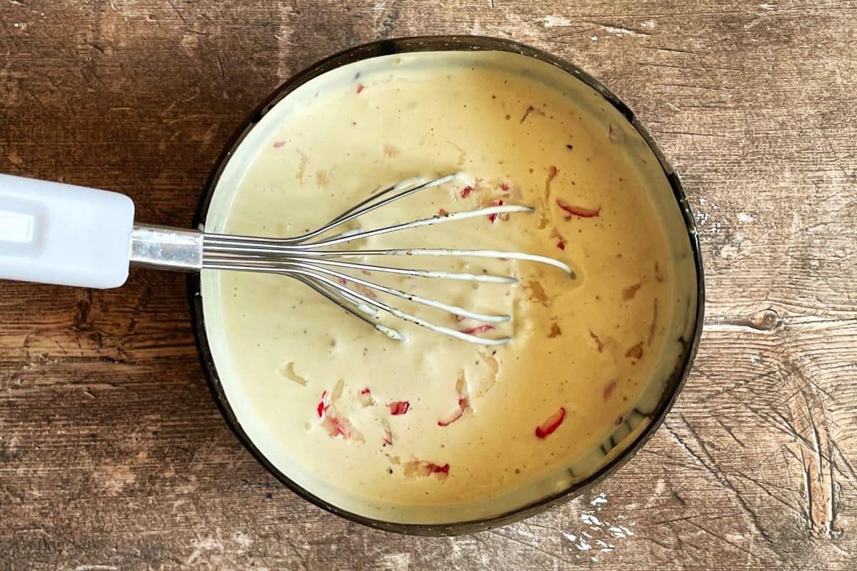 Creamy garlic and radish dip in bowl with whisk.