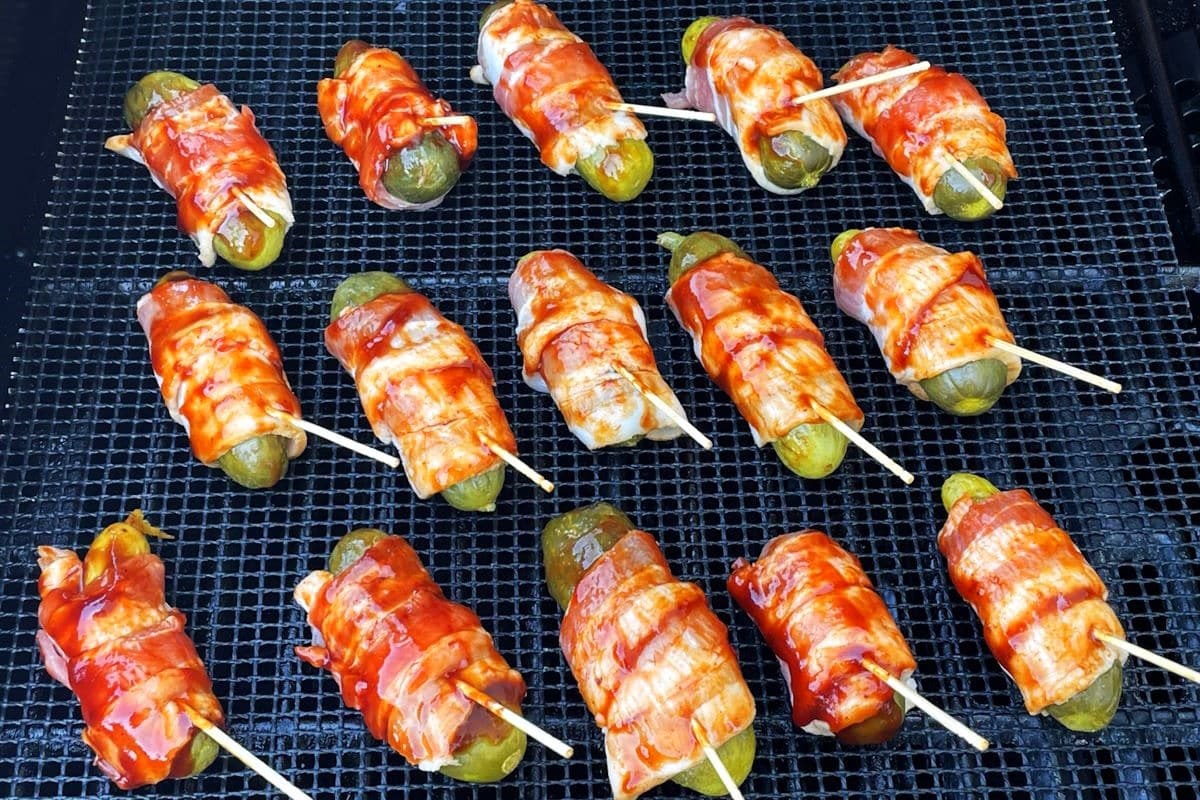 Bacon wrapped pickles on grill mat over indirect heat.