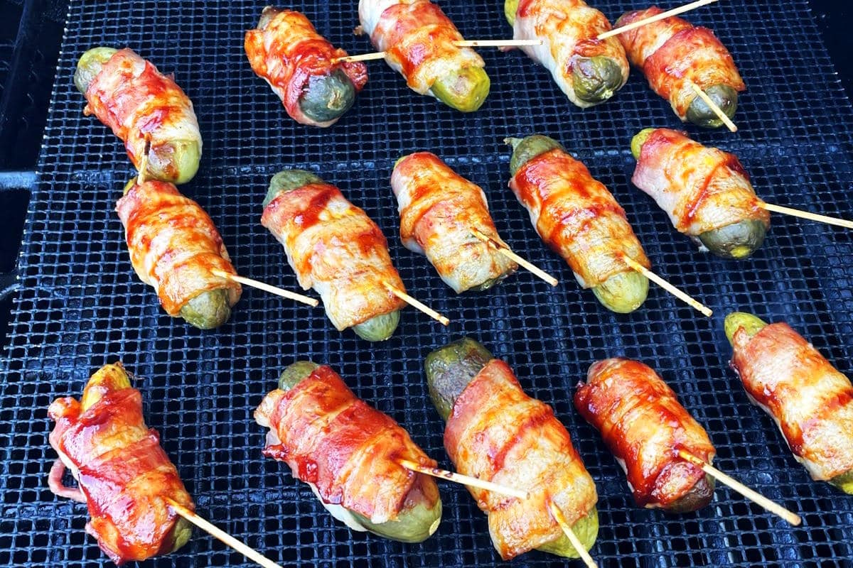 Bacon wrapped pickles on grill mat over direct heat.