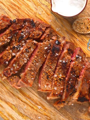 Grilled bison ribeye steak sliced on cutting board with spices on the side.