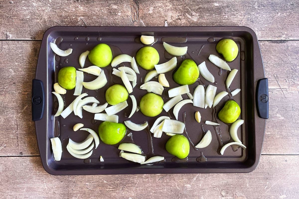 Tomatillos, onions and garlic on sheet pan drizzled with olive oil.