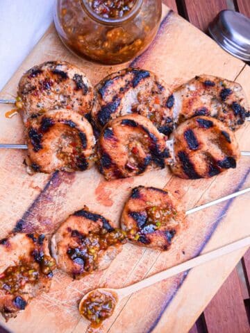 Grilled jerk pork tenderloin skewers on serving board with jerk sauce on the side.