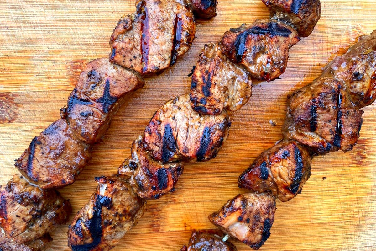 Grilled jerk pork tenderloin skewers resting on cutting board.