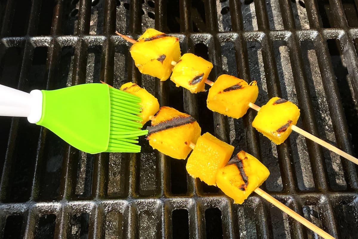 Mango skewers on grill getting brushed with marinade.