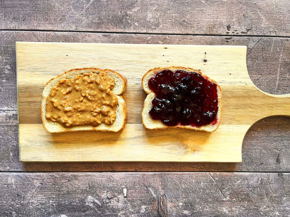 Slices of bread on cutting board with peanut butter and jelly.