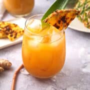 Grilled pineapple juice in stemless wine glass with grilled pineapple wedge garnish.