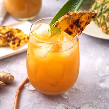 Grilled pineapple juice in stemless wine glass with grilled pineapple wedge garnish.