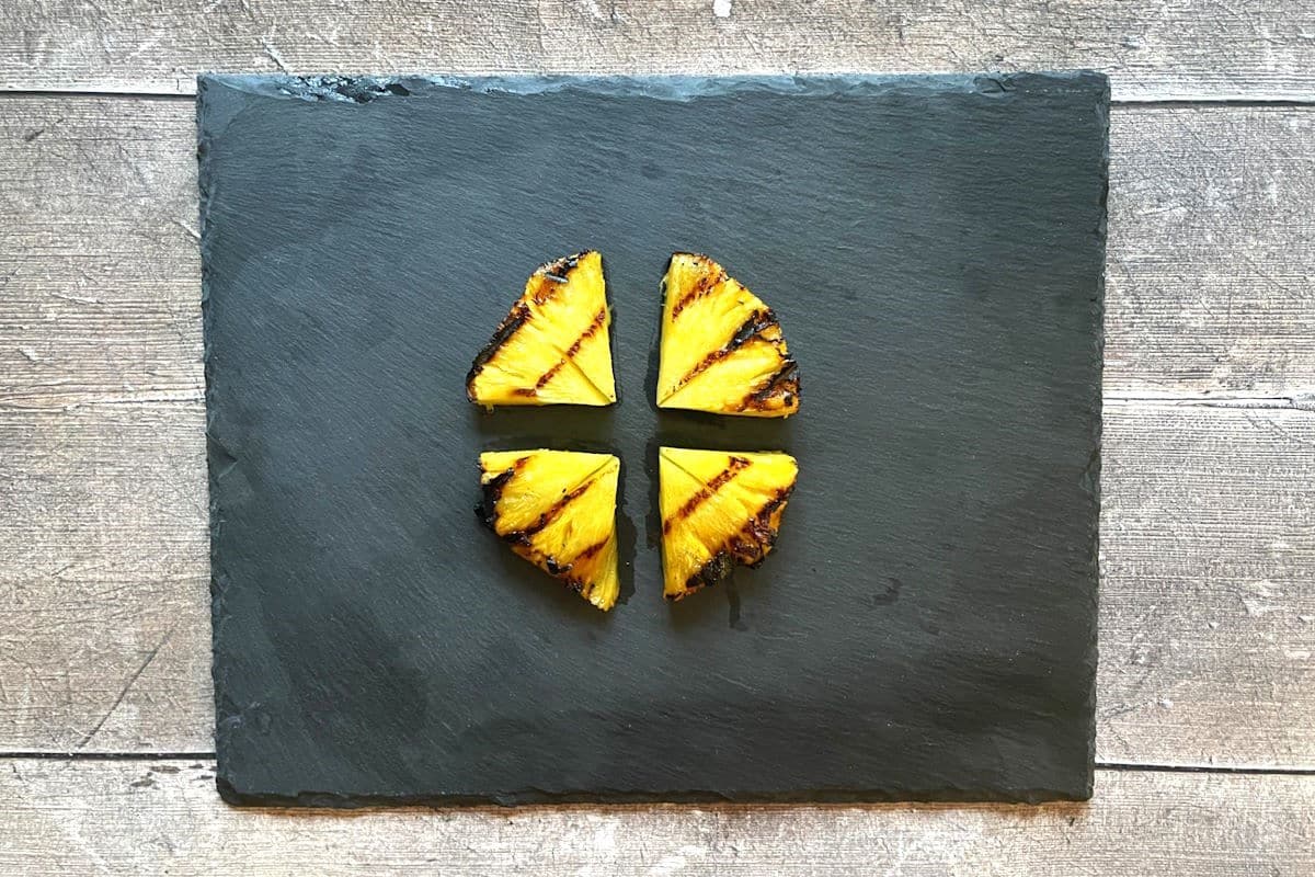 Grilled pineapple garnishes on black board.