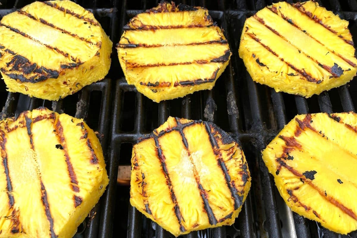 Grilled pineapple slices on outdoor grill.