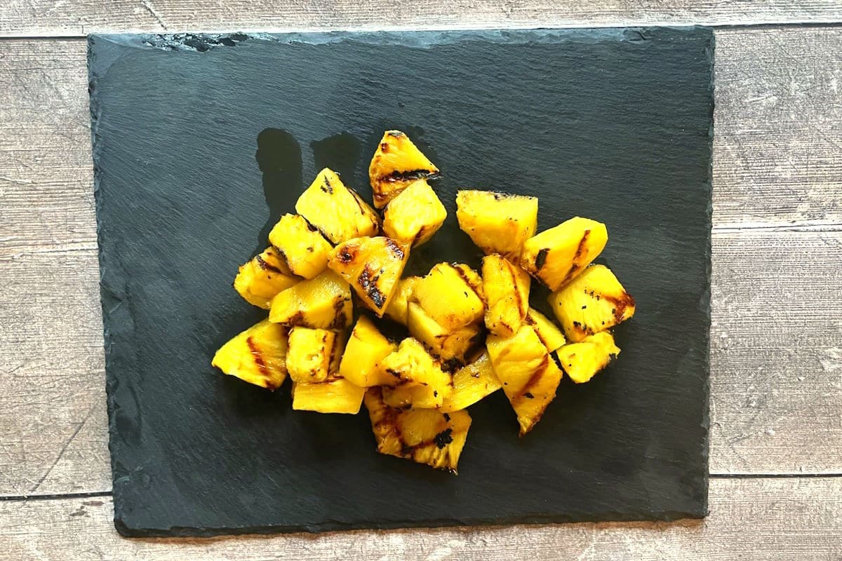 Grilled pineapple chunks on black board.