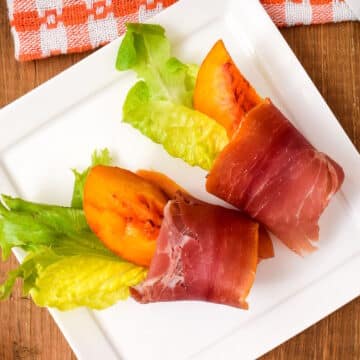 Grilled peaches wrapped in prosciutto on serving dish.