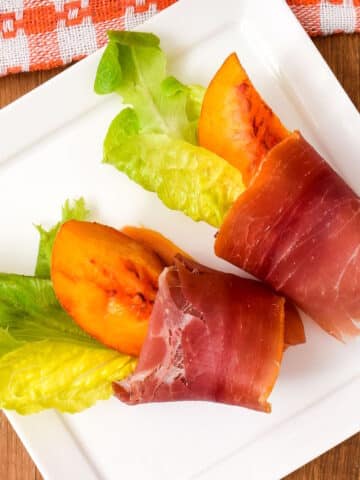 Grilled peaches wrapped in prosciutto on serving dish.