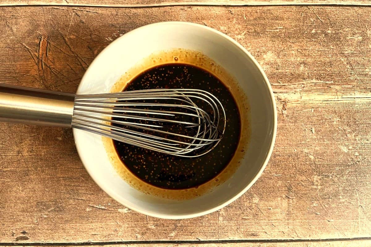 Balsamic dressing ingredients in bowl with whisk.