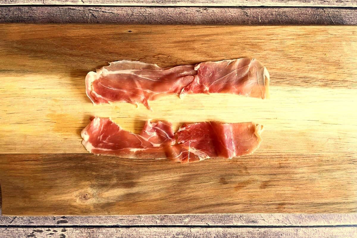 Prosciutto sliced in half on cutting board.