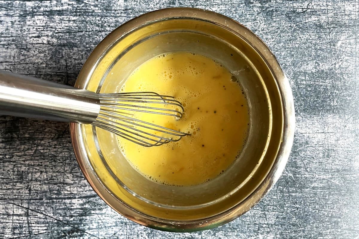 Raw egg mixture in bowl with whisk.