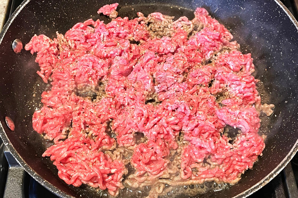 Raw ground beef in pan, crumbled.