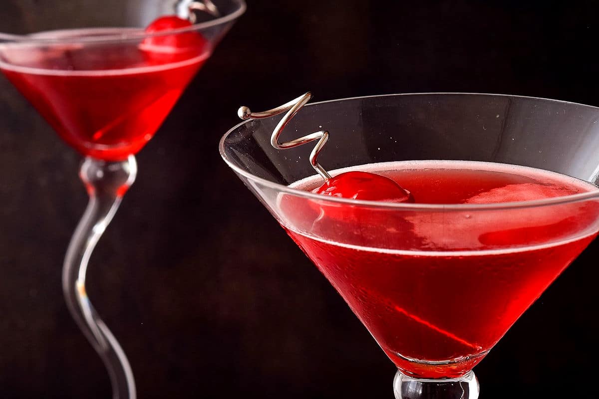 Hibiscus cosmo in martini glass with cherries on black background.
