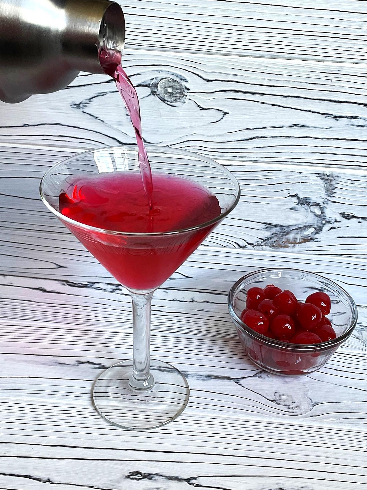 Hibiscus tea cosmo pouring out of cocktail shaker into martini glass.