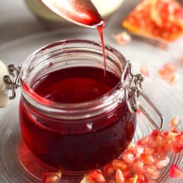 Grenadine syrup pouring from spoon into small glass jar.