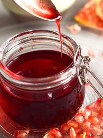 Grenadine syrup pouring from spoon into small glass jar.