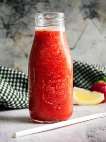 Strawberry juice in a glass jar with a white straw on the side.