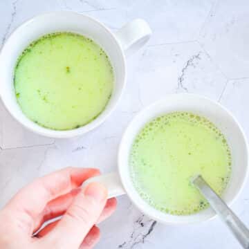 Matcha latte in mugs with spoon.