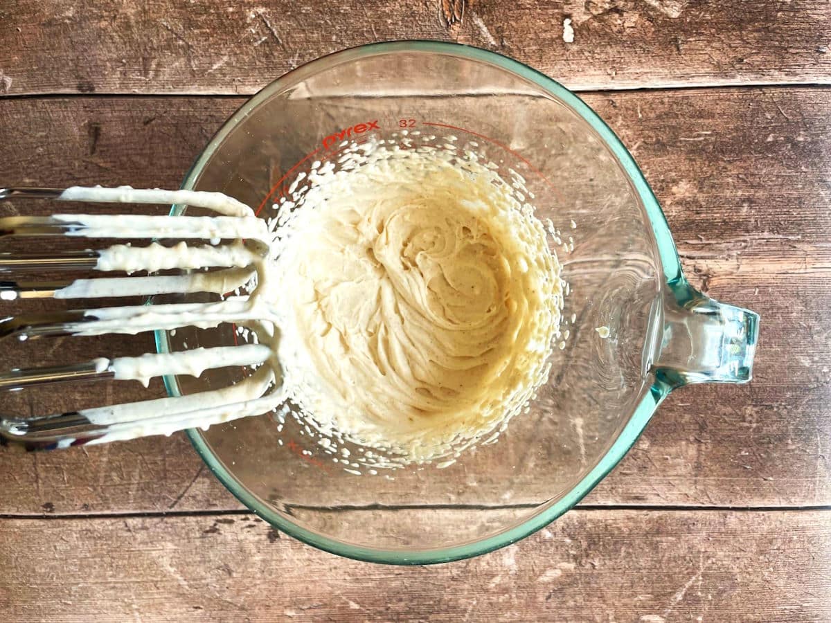 Pumpkin pie spice whipped topping in measuring glass with electric mixer.