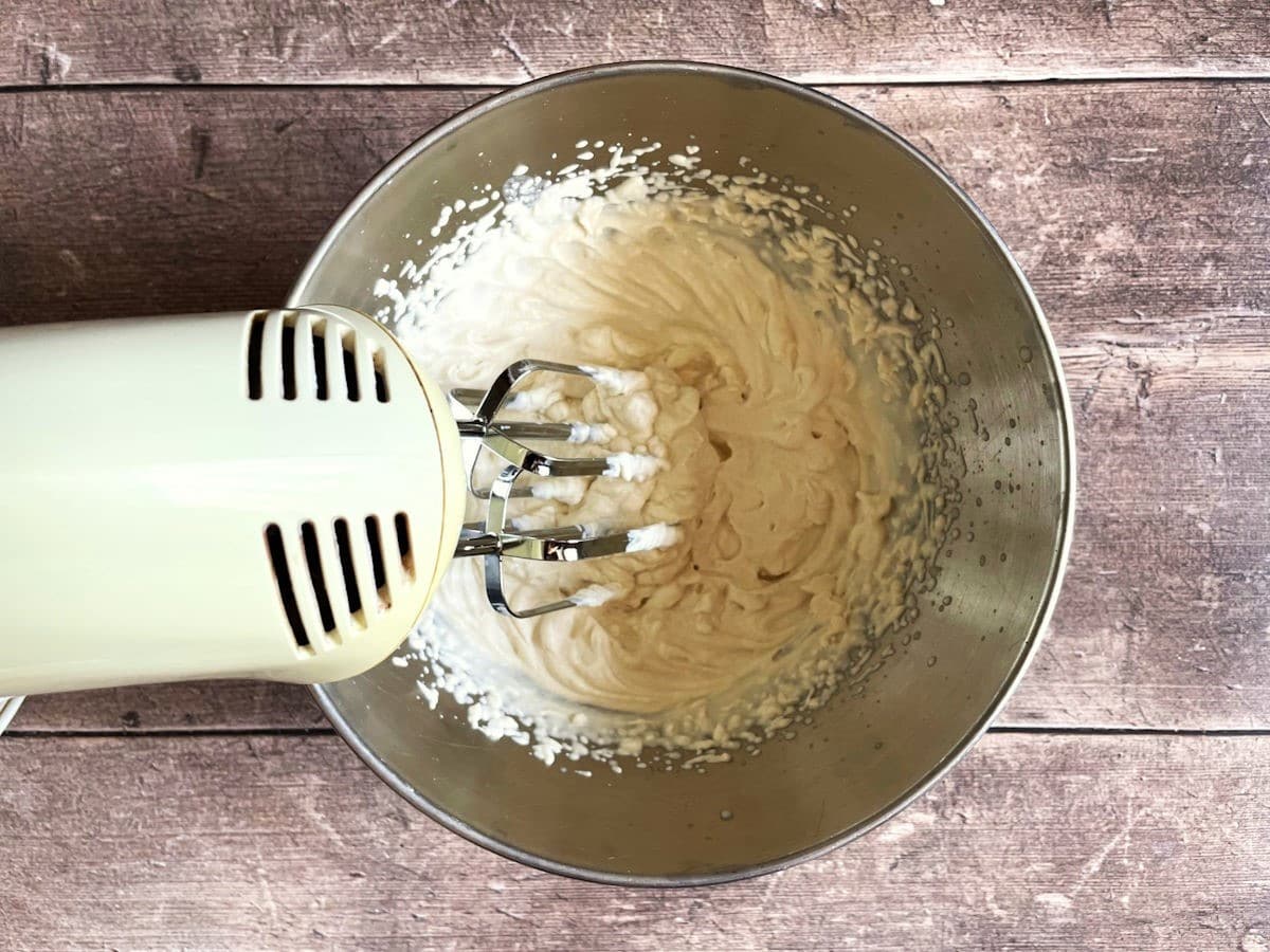 Sweet bourbon whipped topping in bowl with electric whisk.