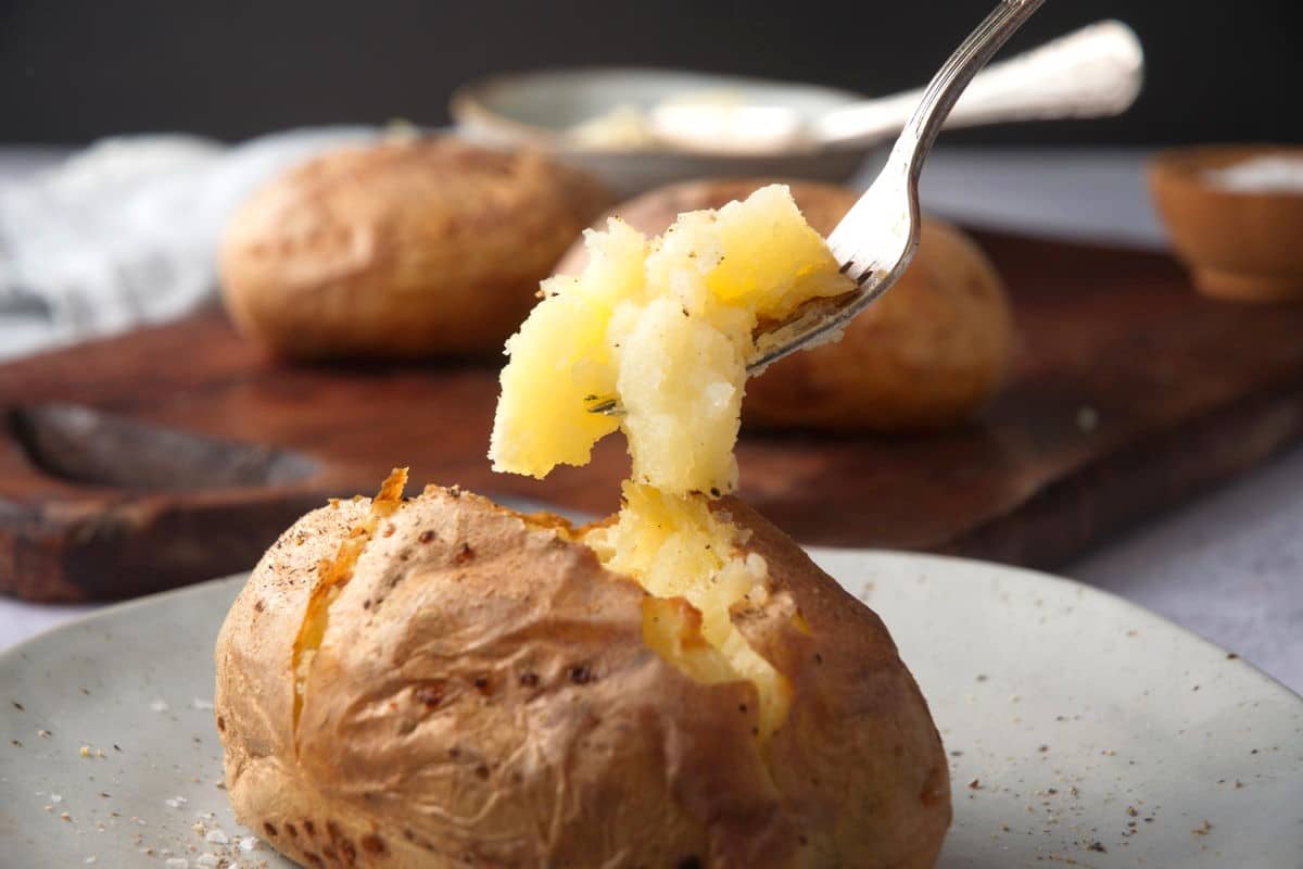 Baked potato on plate with fork in it.