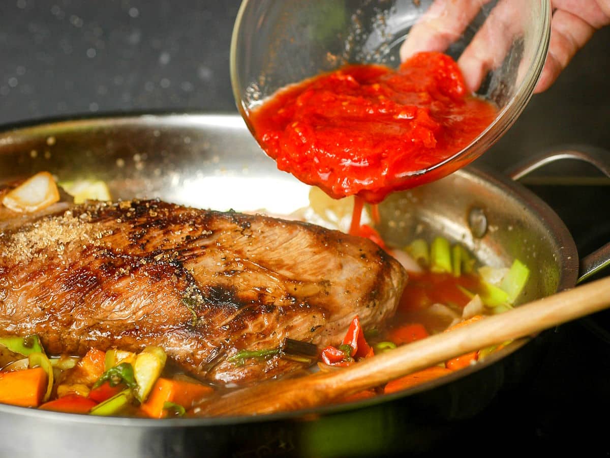 Braised beef in pan with vegetables and tomato puree.
