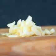 Chopped garlic on cutting board with blue background.