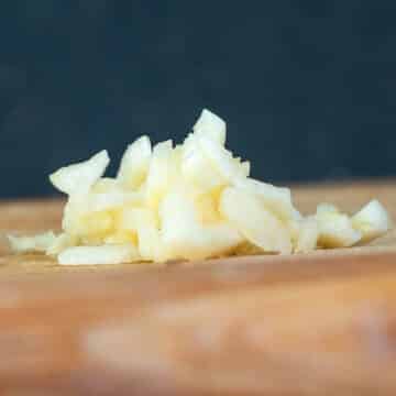 Chopped garlic on cutting board with blue background.