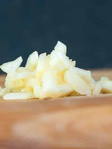 Chopped garlic on cutting board with blue background.