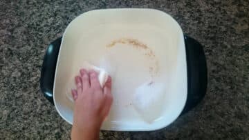 Electric skillet getting cleaned with paper towel and soapy water.