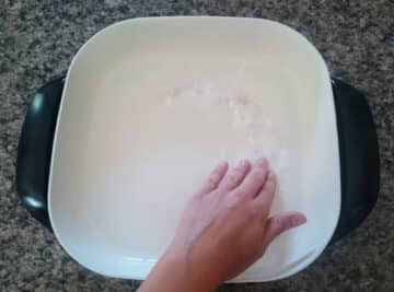 Electric skillet with baking soda paste and a hand.