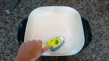 A hand with brush scrubbing electric skillet with baking soda paste.