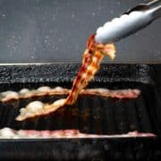 Crispy bacon in grill pan with tongs.